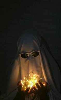 a person wearing sunglasses and a white cloth covering their face with lights in front of them