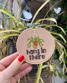 someone holding up a cross stitch ornament that says hang in there