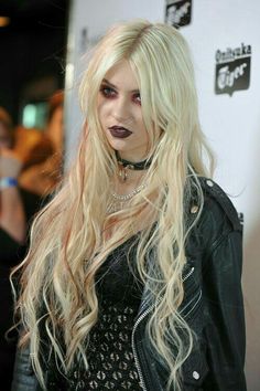 a woman with long blonde hair and black lipstick on her face wearing a leather jacket