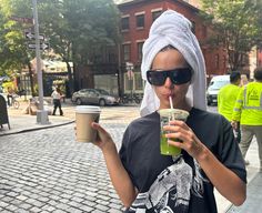 a woman with a towel on her head is drinking from a cup while wearing sunglasses