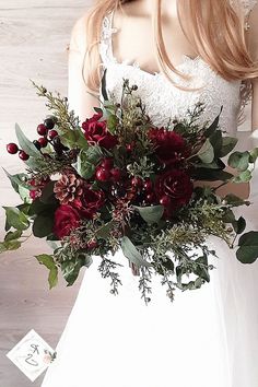 a woman wearing a white dress holding a bouquet of red flowers and greenery in her hand