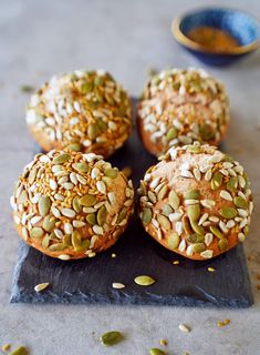 four muffins with sprinkles and seeds are on a slate board