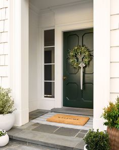 a green front door with a wreath on it and two potted plants next to it