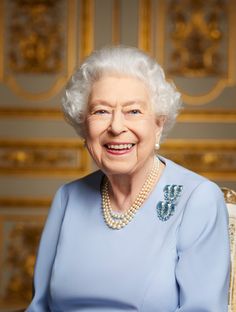 an older woman wearing a blue dress and pearls smiles at the camera while sitting in a chair