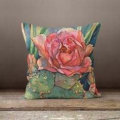 a decorative pillow with an image of a pink flower on it sitting on a wooden table