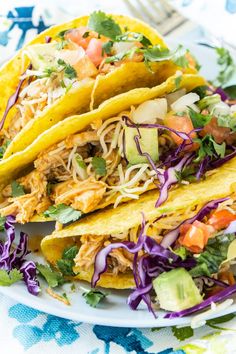 three tacos with shredded cabbage, avocado and tomatoes on a white plate