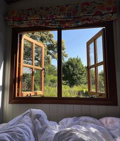 an open window in a bedroom with white sheets on the bed and trees out side