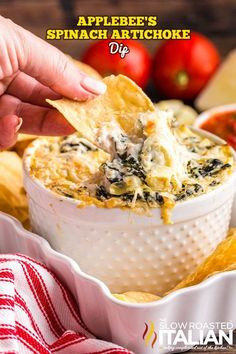 a hand dipping a tortilla chip into a white bowl filled with spinach artichoke dip