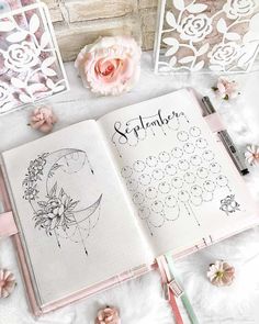 an open planner book sitting on top of a table next to some flowers and pens