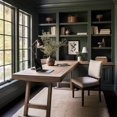 a desk with a laptop on it in front of some bookshelves and windows