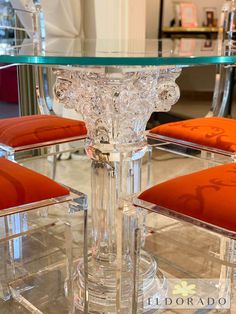 a glass table with four chairs around it and an orange cushion on the backrest