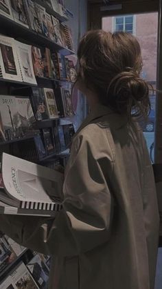 a woman in a trench coat is looking at books on the shelves with magazines behind her