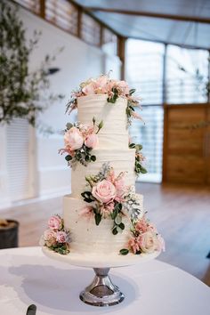 a white wedding cake with pink flowers and greenery on top sits on a table