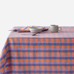 an orange and blue checkered table cloth with two cups on it, next to a white bowl