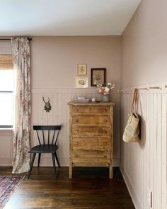 a room with a chair, dresser and pictures hanging on the wall next to a window