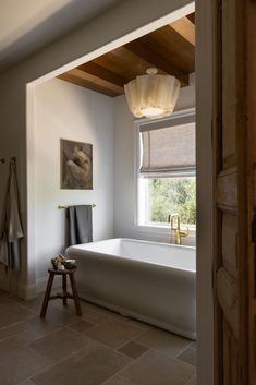 a bathroom with a large bathtub sitting under a window next to a wooden stool