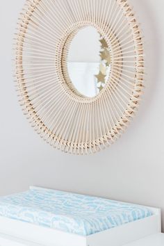 a round mirror hanging on the wall above a white dresser with a blue and white bed