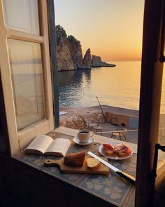 an open window overlooking the ocean with bread, fruit and coffee in front of it