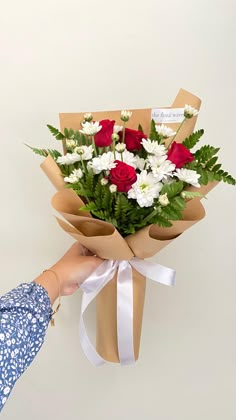 a person holding a bouquet of flowers in their hand with white and red flowers on it