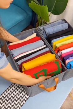 a woman is packing clothes in a suitcase on a table next to a plant and blue couch