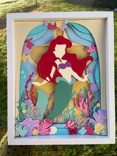 the little mermaid cutout is displayed in a shadow box with seaweed and corals