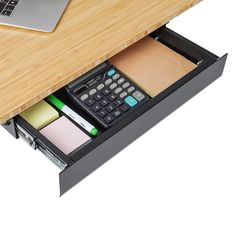 a calculator and pen are sitting in a drawer under a desk with a laptop on it