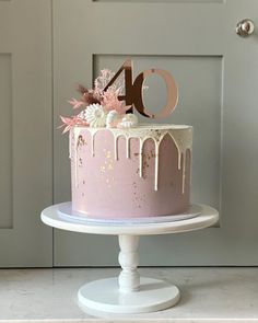 a pink cake with white icing and flowers on top is displayed in front of a door