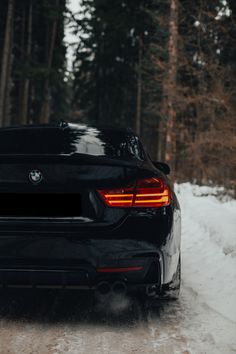 the back end of a black bmw car driving on snow covered road in front of trees