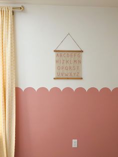 a pink and white room with a wooden sign on the wall next to a window