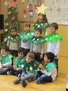 a group of young children wearing green and yellow christmas tree costumes in front of a christmas tree