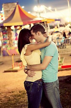 a man and woman embracing each other in front of an amusement park ride at night