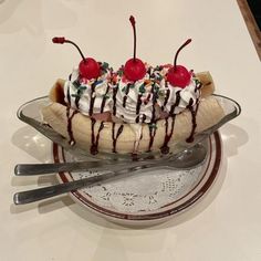 a banana split with ice cream and cherries on it sitting in a glass bowl