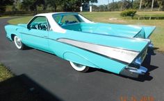 an old blue car parked on the side of a road in front of a field