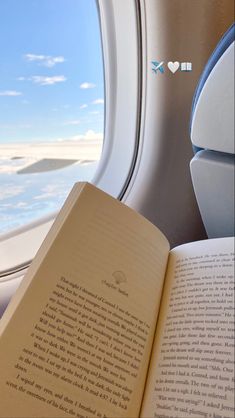 an open book sitting on top of an airplane seat next to a window with the ocean in the background