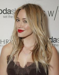 the actress is wearing red lipstick and long blonde hair, while she wears a brown dress