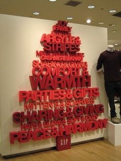 a man standing next to a christmas tree made out of red letters on a white wall