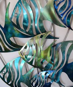 three metal fish hanging on a wall next to each other in blue and green colors