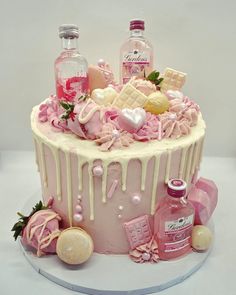 a pink cake with white icing and decorations on the top is surrounded by liquor bottles