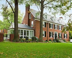 a large red brick house with white trim and windows on the front, surrounded by trees