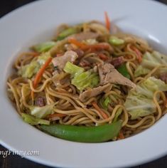 a white bowl filled with noodles and meat on top of a wooden table next to a green pepper