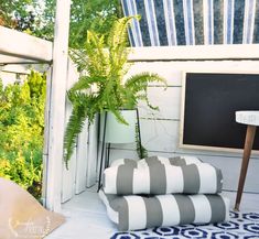 there is a blackboard on the porch next to some pillows and a potted plant