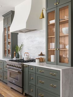 a kitchen with green cabinets and marble counter tops, gold pulls on the oven hood