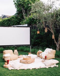 an outdoor movie is set up on the grass in front of a large screen and wicker furniture