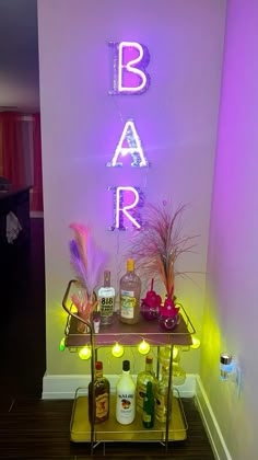 a bar cart with liquor bottles and candles on it in front of a neon sign