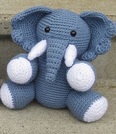 a crocheted stuffed elephant sitting on top of a wooden floor next to a wall