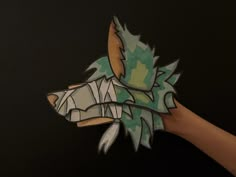 a hand holding an origami animal head with leaves on it's back