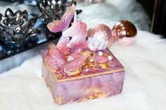 a pink and gold box sitting on top of a white fur covered floor next to ornaments