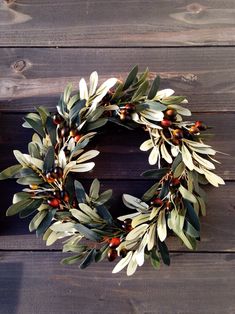 a wreath with olives and red berries hanging on a wooden wall, ready to be used as an ornament