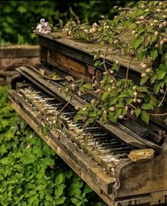 an old piano sitting in the grass with flowers growing out of it's top