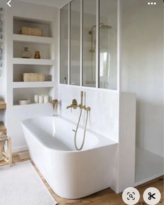 a bathroom with a large white bathtub next to a wooden floor and shelves on the wall